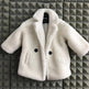 White fluffy coat with black buttons on a hanger against a geometric patterned wall.