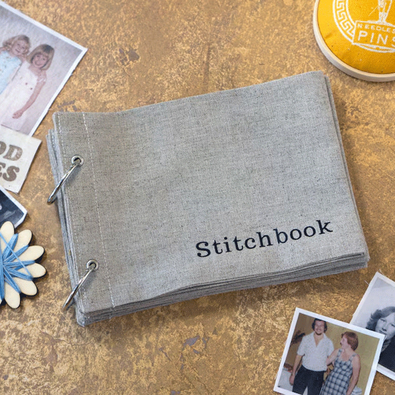Gray 'Stitchbook' on a textured surface with scattered photos and a yellow container.