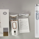 White beauty wand device shown with its retail box, charging cable, and instruction manual on a light gray background.