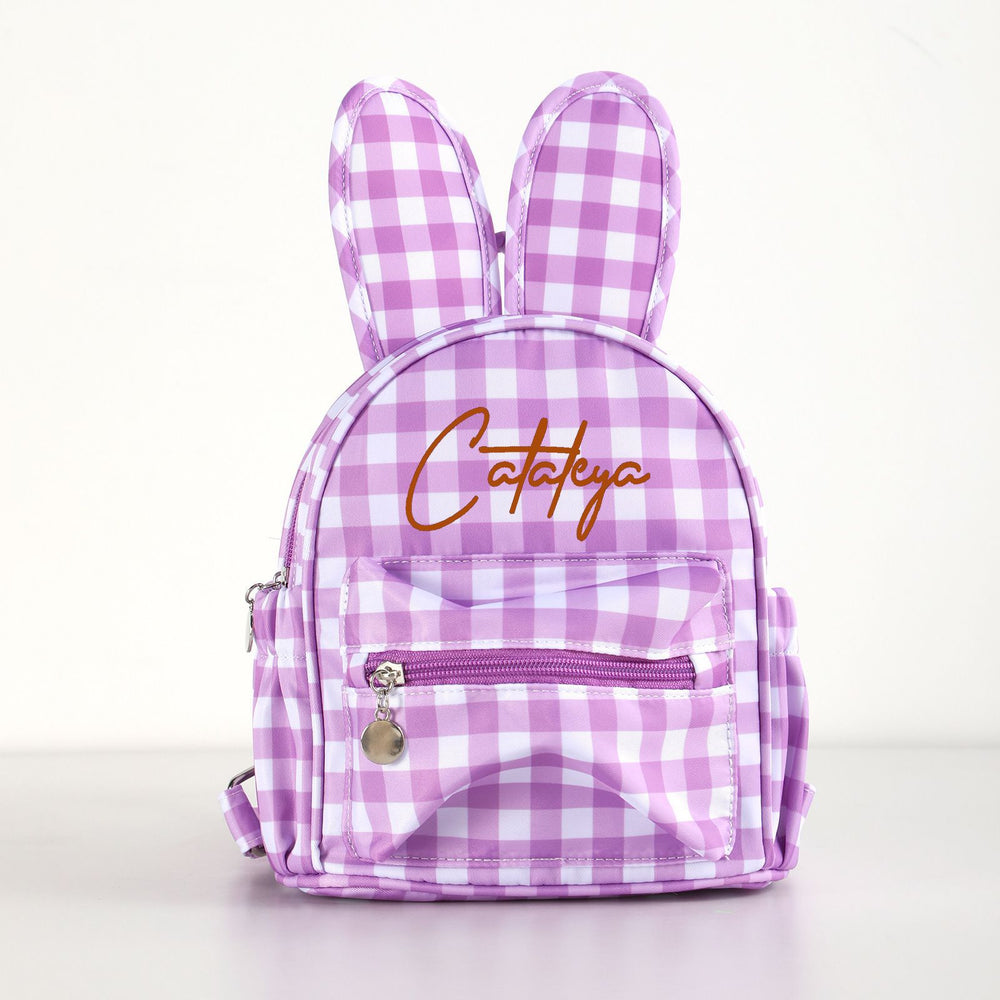 A small bunny-shaped backpack in a pink and white gingham pattern, featuring embroidered brown cursive text reading 'Catalya' on the front pocket, photographed against a clean white background.