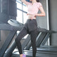 A woman posing on a treadmill in a gym, wearing a light pink short-sleeve crop top, black high-waisted athletic leggings, and purple athletic sneakers.