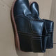 A pair of black leather ankle boots with white contrast stitching and brown soles, shown on a plain cardboard background.