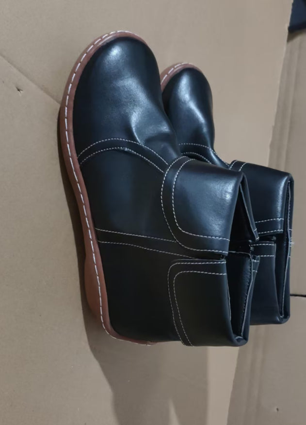 A pair of black leather ankle boots with white contrast stitching and brown soles, shown on a plain cardboard background.