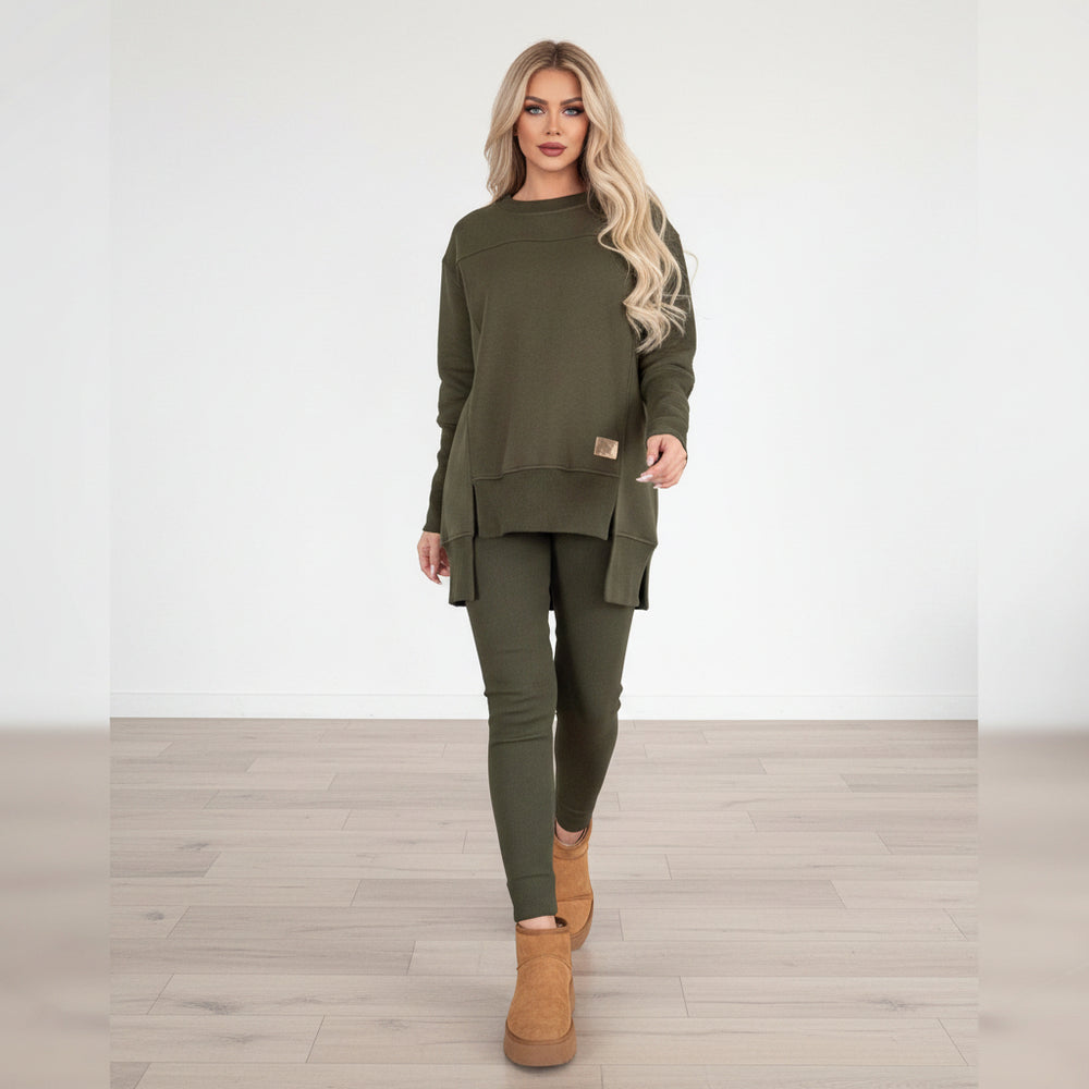 Woman wearing a green outfit with beige boots standing in front of a staircase.