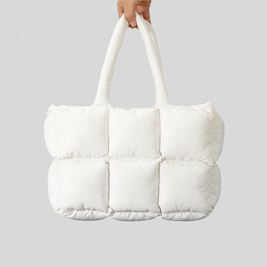 White quilted tote bag held by a hand on a light gray background