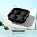 Black silicone four-ball ice mold tray shown on a white plate with two small green limes, on a light blue background. Red text reads '2pcs' and a gray label reads 'Four-ball black' with dimensions below.