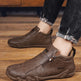 Brown leather shoes with a brand logo worn by a person on a wooden floor.