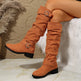 Brown knee-high boots with buckles worn by a person sitting on a textured surface.