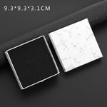 Two square boxes, one black and one with a white marble pattern, on a dark surface.