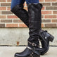 Black leather boots with buckles worn by a person against a brick wall.