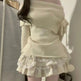 Woman wearing a light-colored off-shoulder top and ruffled skirt against a neutral background