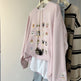 Pink sweatshirt with embroidered designs on a hanger against a neutral background