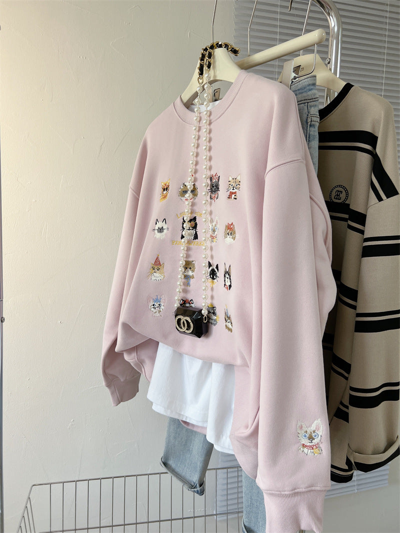 Pink sweatshirt with embroidered designs on a hanger against a neutral background