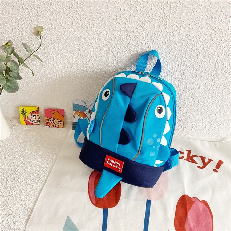 Blue dinosaur-shaped backpack on a textured white wall with decorative elements.