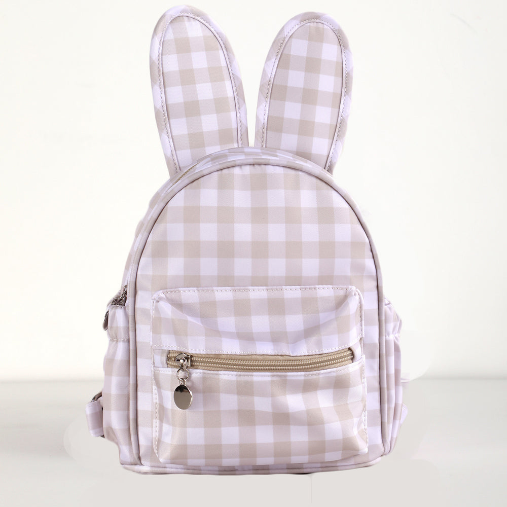 A small bunny-shaped backpack with long ears, featuring a beige and white gingham check pattern and a front zippered pocket with a gold zipper pull.