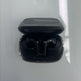 Open black wireless earbuds charging case with the earbuds inside, photographed from above on a glossy white surface with soft window light reflections.