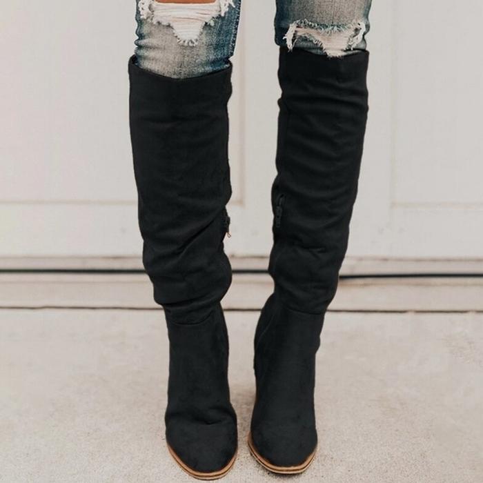 Black knee-high boots worn with ripped jeans on a neutral background