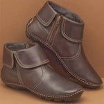 Pair of brown leather ankle boots with a zipper on a beige background