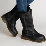 Black leather boots worn with blue jeans on a light gray background