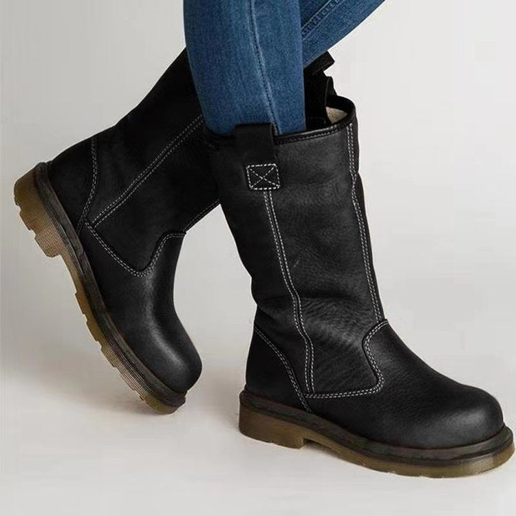 Black leather boots worn with blue jeans on a light gray background
