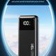 A black portable power bank with a digital display showing 100% battery level, set against a blue sky background with a circular frame and promotional text about travel.