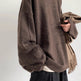 Person wearing a brown oversized sweater holding a beige coat against a white background