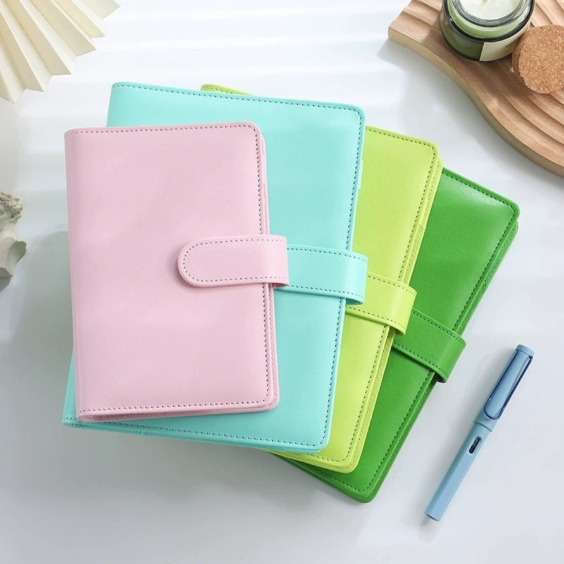 Three colorful planners stacked with a pen on a light surface
