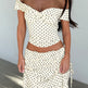 Woman wearing a polka dot off-shoulder top and skirt set against a plain background