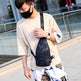 Person wearing a beige shirt and white pants with a black camouflage sling bag outdoors.