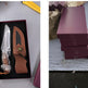 Knife with sheath in a box on a gray surface, next to stacked purple boxes.
