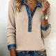 Woman wearing a beige sweater with denim accents and blue jeans on a plain background