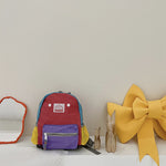 Colorful backpack with a purple compartment, red top, and yellow accents on a white surface.