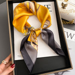Yellow and black patterned silk scarf in a box with a hand holding it.