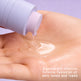 Hand holding a small container of cream with a light purple background