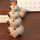 A stack of four small wooden bear figurines with dark brown snouts and noses, arranged on a wooden tabletop. The top bear has a small orange pom-pom on its head.