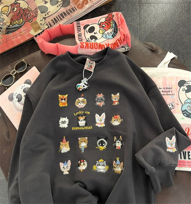 Black sweatshirt with cat illustrations on a table with books and sunglasses.