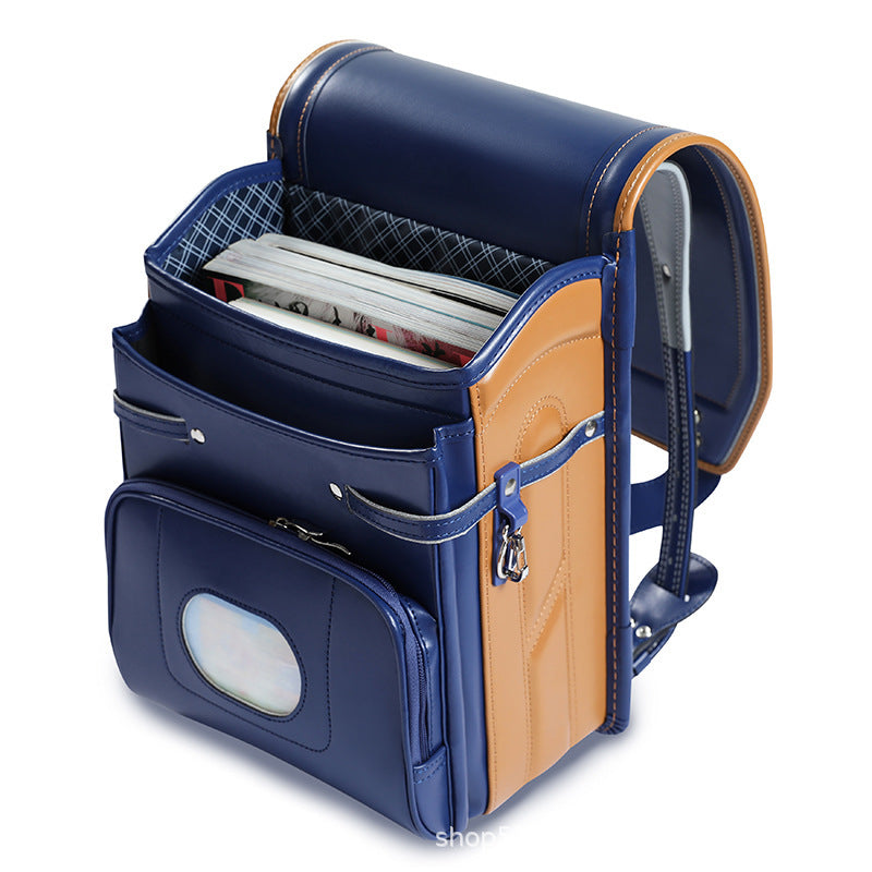 A navy blue and tan school backpack shown open, containing a stack of notebooks or magazines. The backpack features multiple compartments, a front pocket with a clear window, and padded shoulder straps, photographed on a white background.