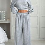 Person wearing a gray off-shoulder top and wide-leg pants in a bedroom setting.