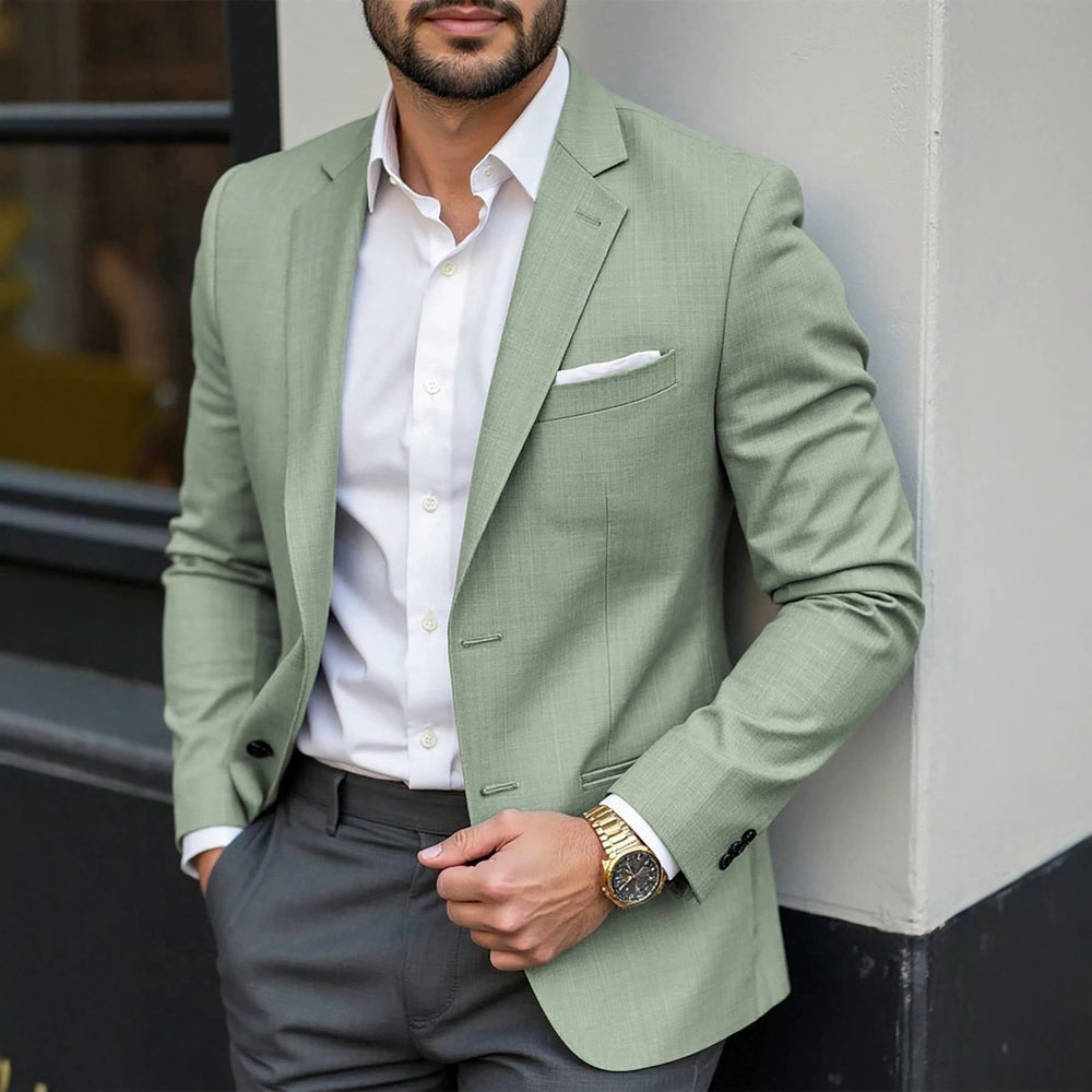 Man wearing a light green blazer over a white shirt with gray pants, standing against a neutral background.