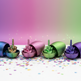Four metallic Easter egg-shaped containers on a white surface with scattered confetti, each cracked open to reveal a small green middle finger figurine inside. The eggs are blue, pink, green, and purple, set against a pink-to-green gradient background.