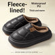 A pair of black fleece-lined slip-on slippers with quilted panels and a soft brown interior, shown on a light beige background with promotional text reading 'Fleece-lined!', 'Waterproof PU Thick and warm', and 'Winter Warm Cotton Slippers'.