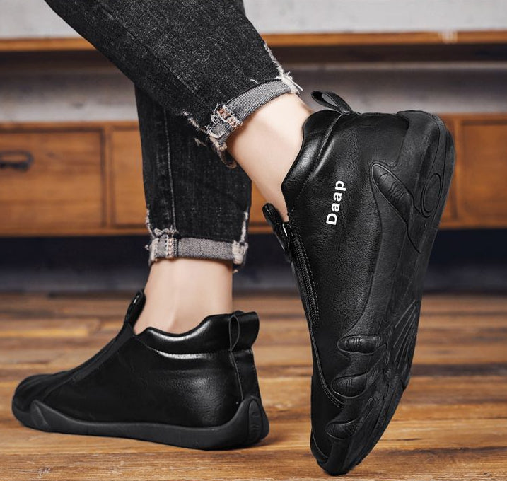 Black slip-on shoes with 'Daap' branding worn by a person on a wooden floor.