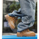 A close-up lifestyle shot of a person wearing light blue distressed jeans and tan bandana-patterned lace-up boots with chunky soles, standing on a bright blue platform outdoors.