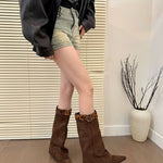 Person wearing brown knee-high boots with leopard print trim in a room with a plant and window blinds.