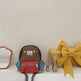 Children's backpack with colorful compartments on a white surface with a yellow bow and small figurines.