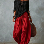 Woman wearing a black off-shoulder top and red harem pants against a gray background
