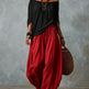 Woman wearing a black off-shoulder top and red harem pants against a gray background