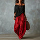 Woman wearing a black top and red pants holding a brown bag against a gray background