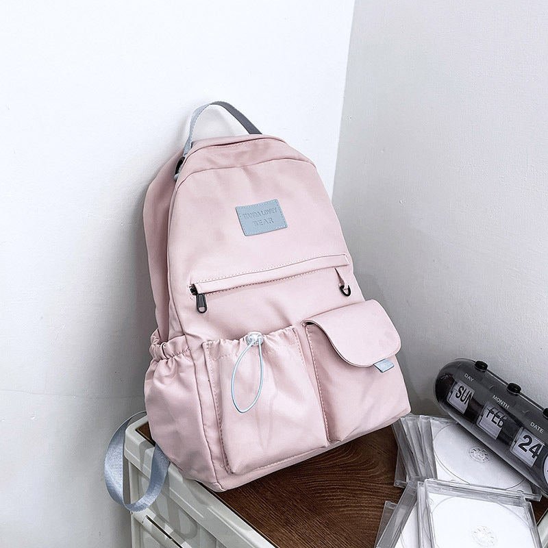 Pink backpack on a white surface with a clock in the background