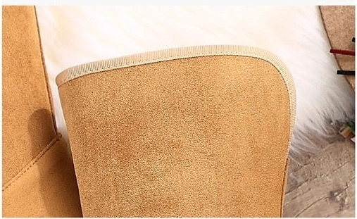 A close-up of a tan suede or microfiber cushion cover with a beige stitched edge, resting on a white faux fur surface.